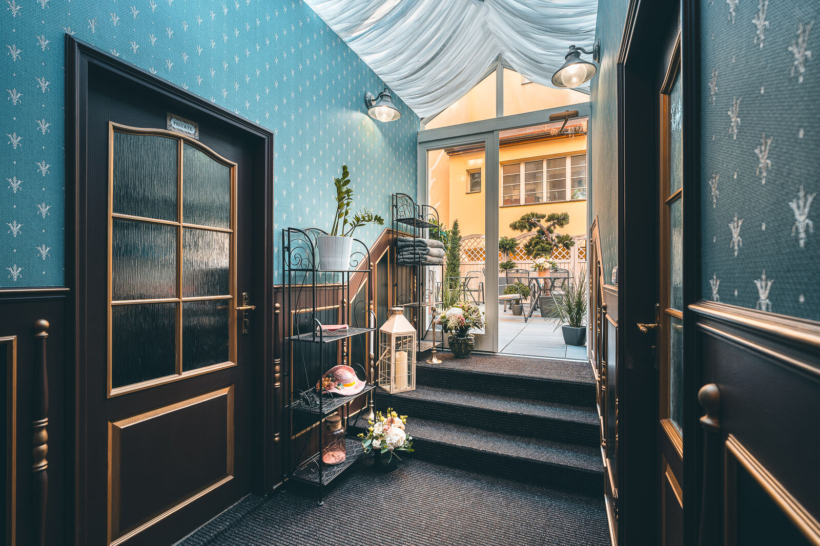 Blue wallpapered corridor at Hotel Haštal Prague leading up a few steps to the sunlit terrace