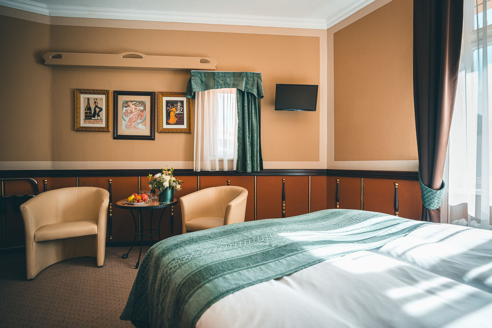 Bright double room with a green bedspread, two armchairs and framed posters at Hotel Haštal Prague