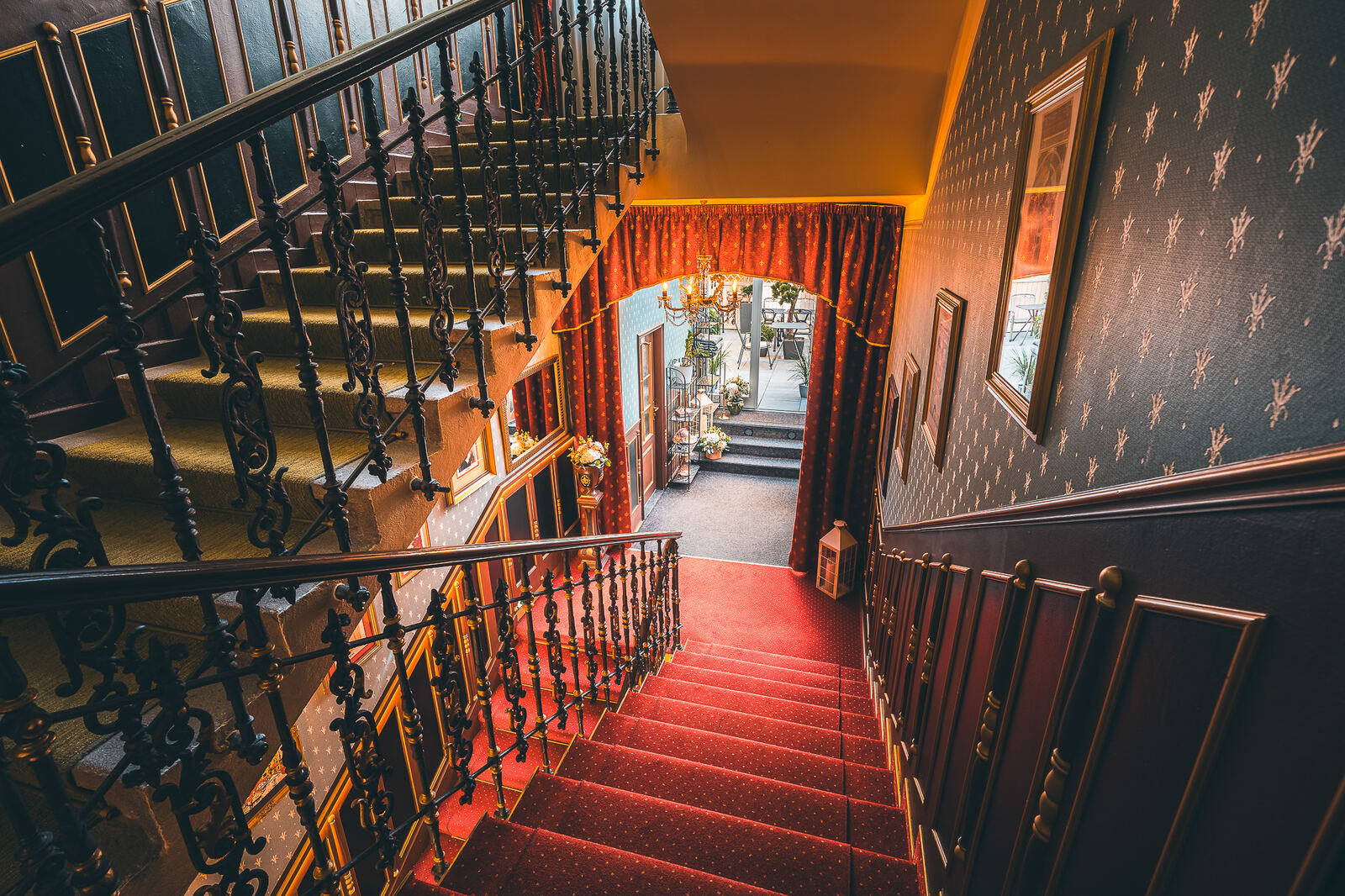 View down a red-carpeted staircase with a wrought-iron railing at Hotel Haštal Prague