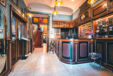 Wood-panelled lobby with a reception desk and red-carpeted staircase at Hotel Haštal Prague