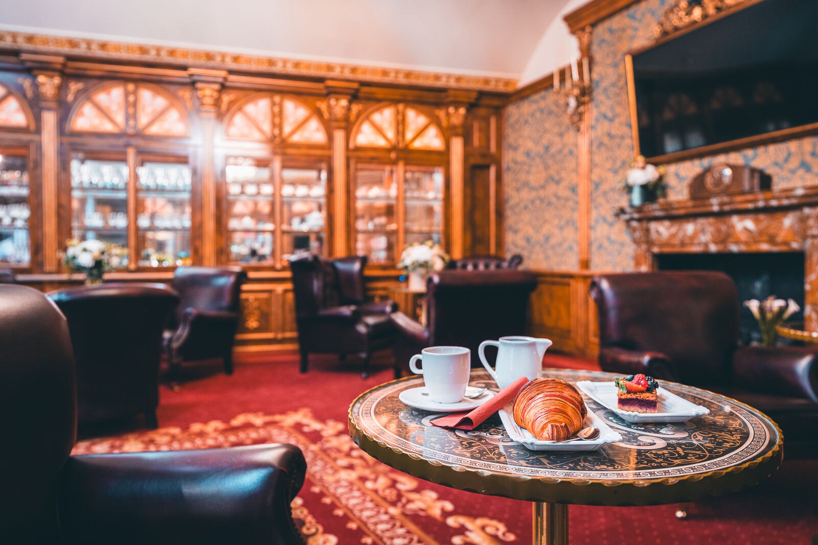 Coffee, croissant and cake on a table in the wood-panelled lounge at Hotel Haštal Prague