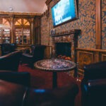 Lounge with leather armchairs, a marble fireplace and patterned wallpaper at Hotel Haštal Prague