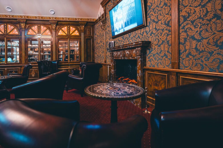 Lounge with leather armchairs, a marble fireplace and patterned wallpaper at Hotel Haštal Prague