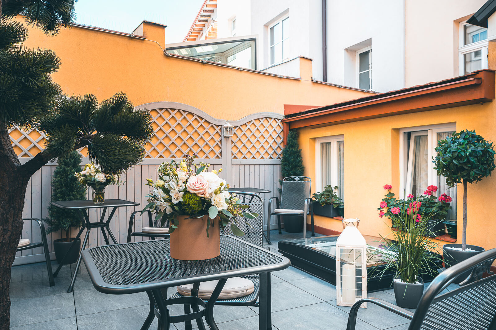 Sunny patio terrace with tables and flowers at Hotel Haštal Prague