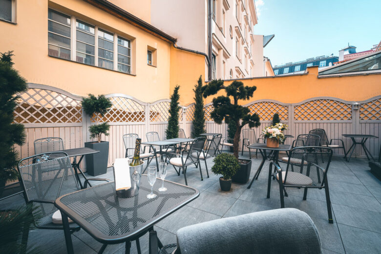 Sunny courtyard terrace with tables, flowers and a champagne bucket at Hotel Haštal Prague