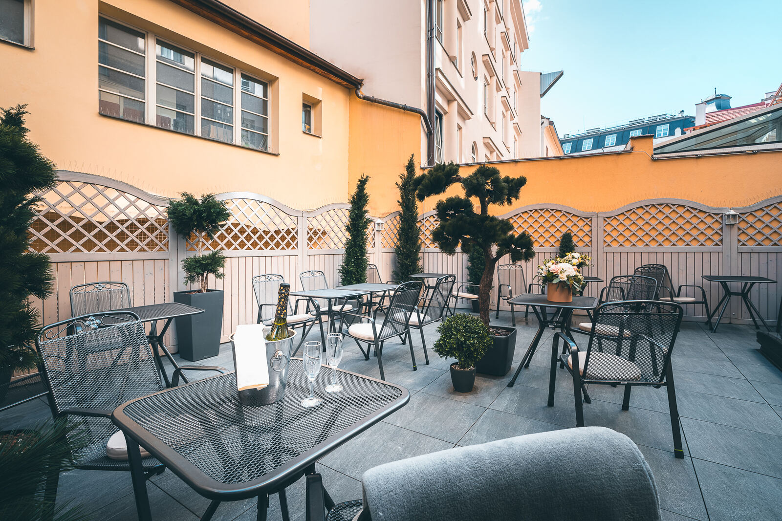 Sunny courtyard terrace with tables, flowers and a champagne bucket at Hotel Haštal Prague
