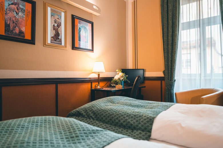 win room at Hotel Haštal Prague with Art Nouveau posters, a desk and green bedspreads