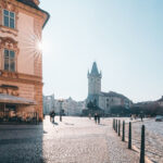 Sunlit cobbled square in Prague Old Town with a historic tower in the distance