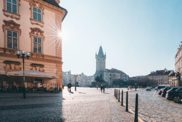 Sunlit cobbled square in Prague Old Town with a historic tower in the distance