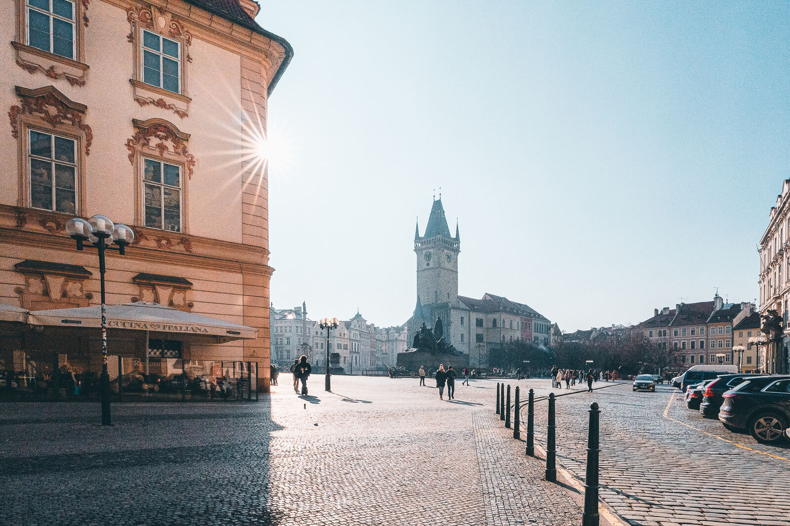Sunlit cobbled square in Prague Old Town with a historic tower in the distance
