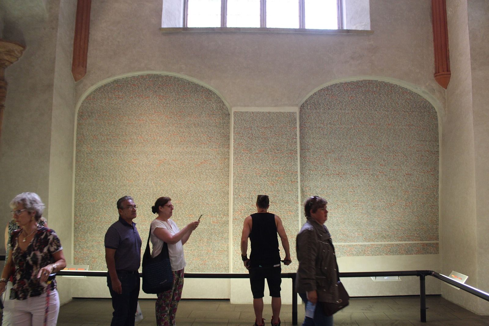 Visitors in front of the memorial wall with victims' names inside the Pinkas Synagogue in Prague